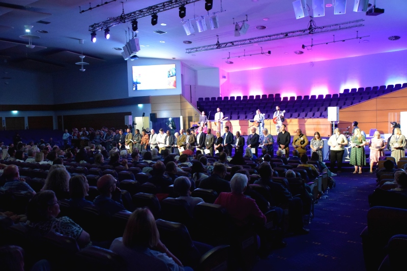 Photo from back of auditorium showing ministers being commissioned standing in a line at the front of the stage