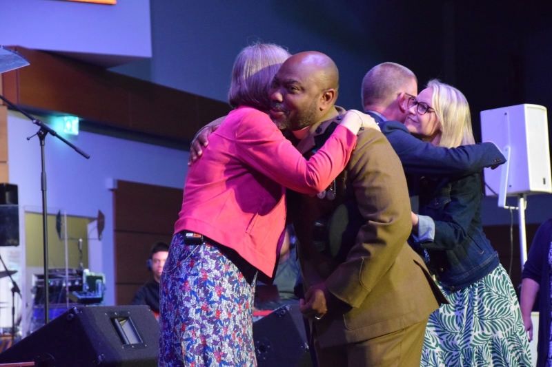 2 newly commissioned ministers - a man and a women - embrace General Secretary Lynn Green and an Association representative on the stage at the Baptist Assembly