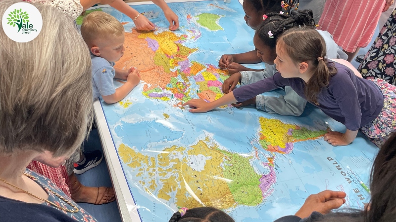Children point to countries on a large global map at Vale Community Church while adults look on