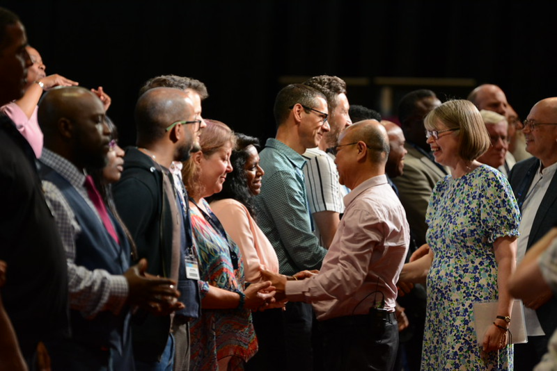 Ministers who have transferred to the accredited list stand in a line and receive handshakes from BMS General Director Kang San Tan and Baptist Union General Secretary Lynn Green at the 2023 Baptist Assembly in Telford