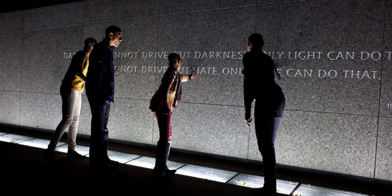 President Barack Obama, First Lady Michelle Obama, and daughters Sasha and Malia tour the Martin Luther King, Jr. Memorial in Washington, D.C., October 14, 2011. They are looking and pointing at a wall which states: "Darkness cannot drive out darkness; only light can do that. Hate cannot drive out hate; only love can do that." They are facing away from the camera