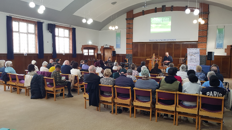 Hub speaker Joe Egan at Oakwood Baptist Church. The photo is taken from the back of the church, showing around 50 people on chairs, listening and taking notes