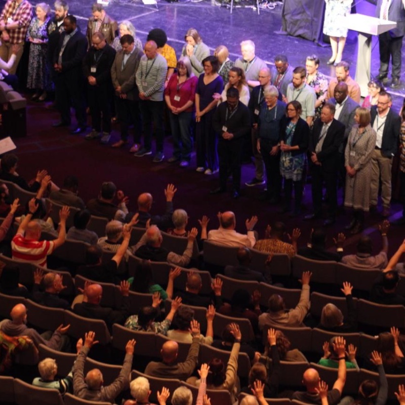 Overhead photo showing the congregation raising their hands in prayer for the ministers being presentated at the front of the stage