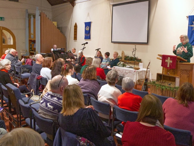 A view from the back of a church congregation watching a woman speak from a wooden pulpit
