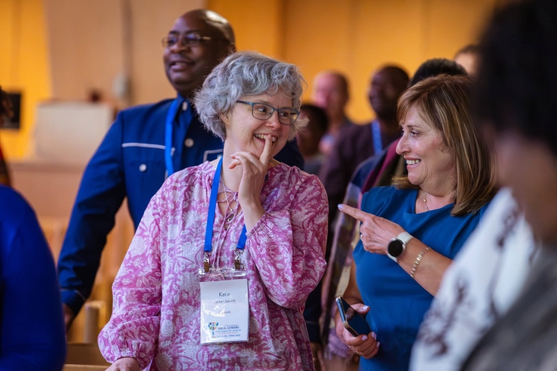 Two women wearing conference lanyards smiling and chatting animatedly in a crowd.